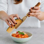 Grating Parmesan cheese over a bowl of freshly prepared Italian risotto garnished with basil and cherry tomatoes