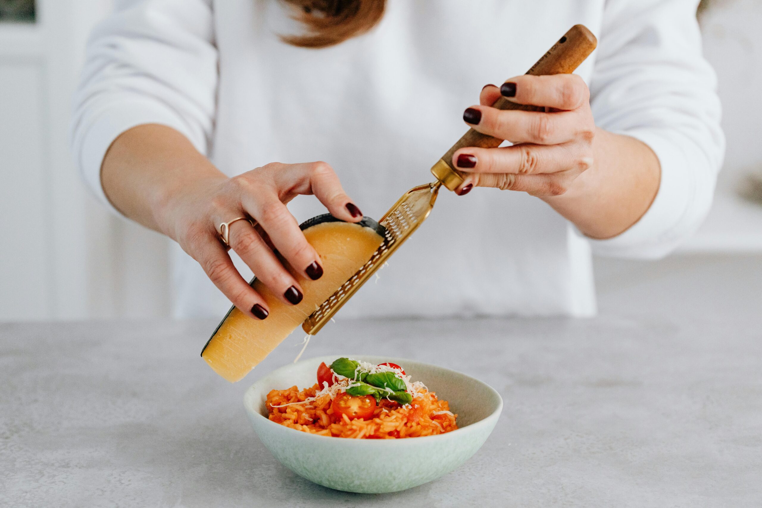 Grating Parmesan cheese over a bowl of freshly prepared Italian risotto garnished with basil and cherry tomatoes