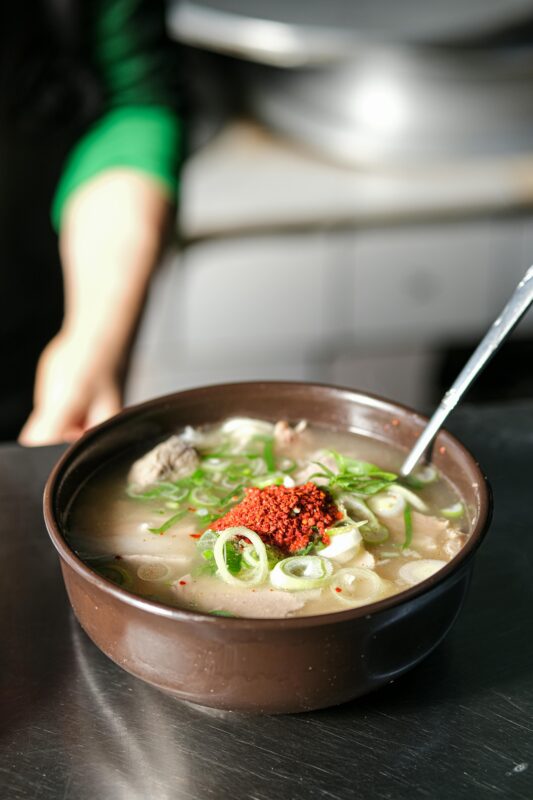 Bowl of Korean beef soup (Seolleongtang) with green onions and red chili flakes, served in a brown bowl with a silver spoon.