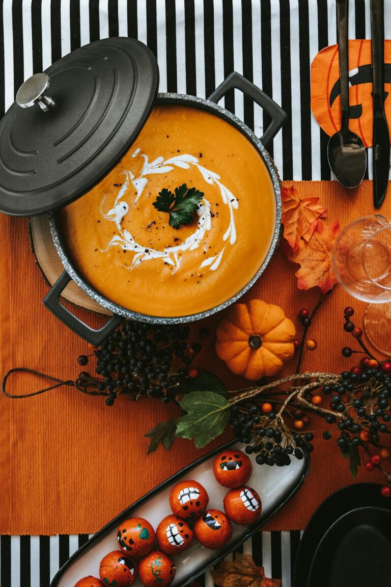 A festive pot of Spicy Korean Pumpkin Soup garnished with cream and parsley, surrounded by pumpkins and autumn-themed decor on an orange and striped background.